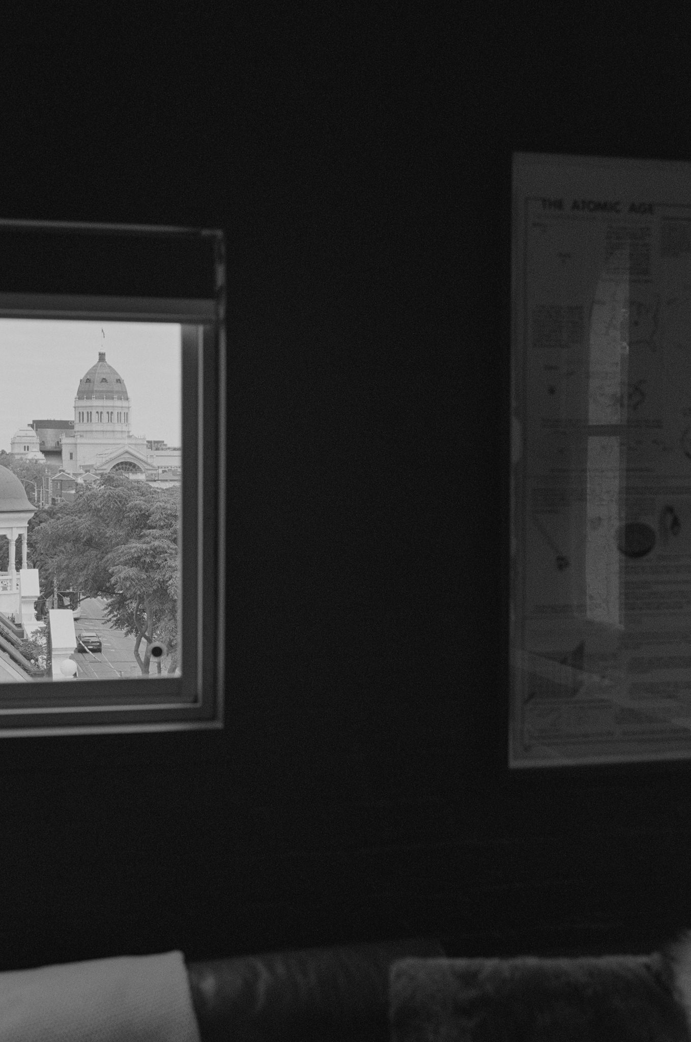 View from an interior room with dark walls, capturing the iconic dome of a historic building through a window. The distant architecture is framed by trees lining the street, adding a sense of depth and contrast to the scene. The window view provides a striking juxtaposition between the modern, moody interior and the classic, timeless beauty of the historic structure outside. A wall-mounted map on the right side adds a touch of intellectual and eclectic decor to the space.
