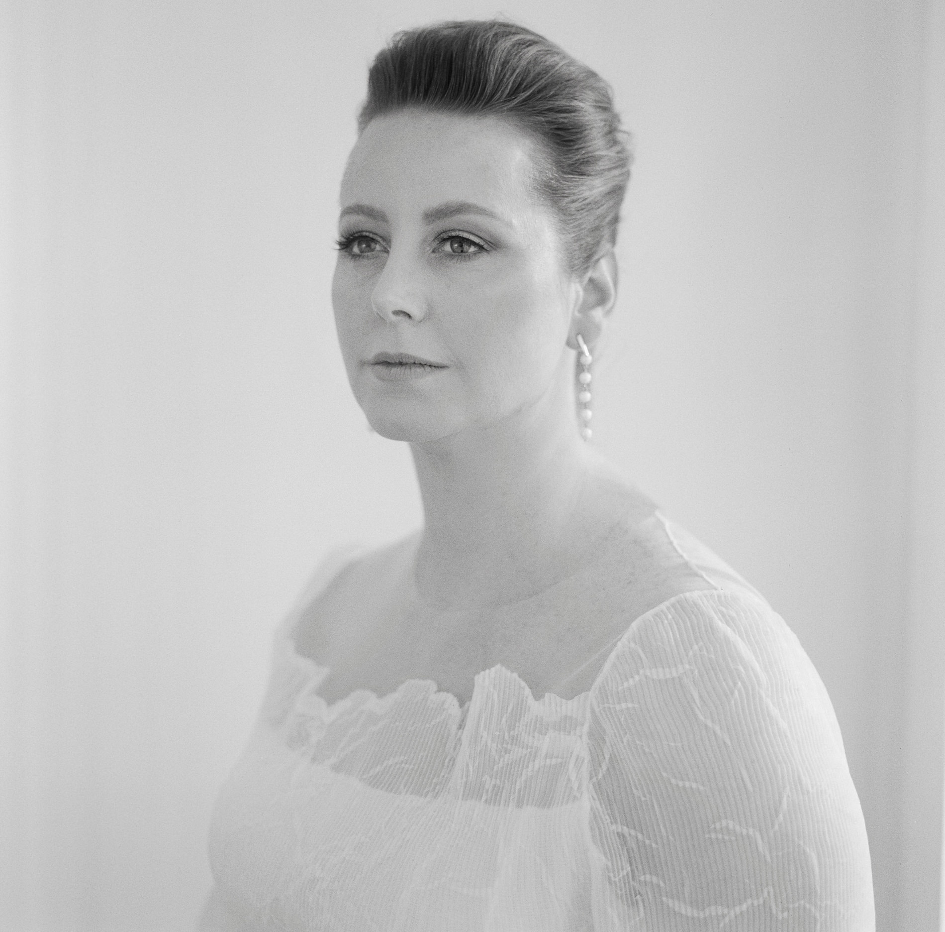 A close-up portrait of the bride at a Rupert on Rupert wedding in Melbourne, captured on medium-format Kodak film. The bride is dressed in a white gown with sheer sleeves and wears pearl drop earrings. She is looking off-camera with a calm and composed expression.
